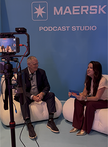 Overhaul-300 A camera on a tripod records an interview at the Maersk Podcast Studio, where two speakers sit on white lounge chairs during Manifest 2026 in Las Vegas.